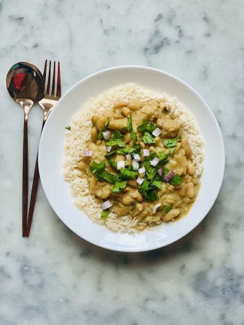 A white bowl of coconut white bean and cauliflower over rice.
