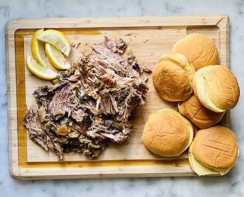 A pile of pulled pork and sandwich buns on a wooden cutting board.