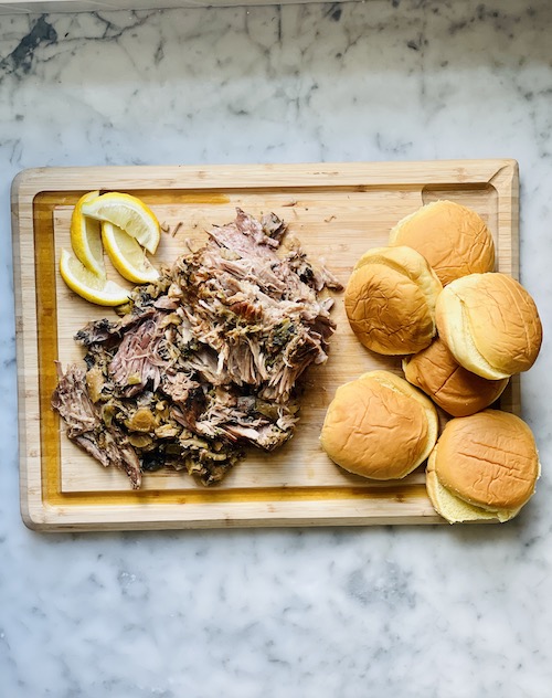 A pile of pulled pork and sandwich buns on a wooden cutting board.