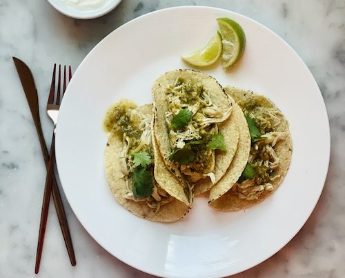 A white plate holding three salsa verde pulled chicken tacos.