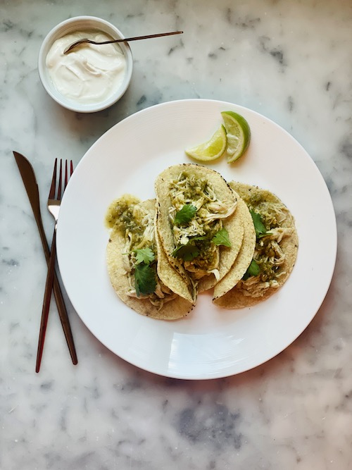 A white plate holding three salsa verde pulled chicken tacos.