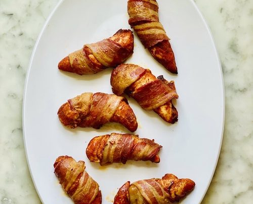 Bacon wrapped chicken tenders on a white serving platter.