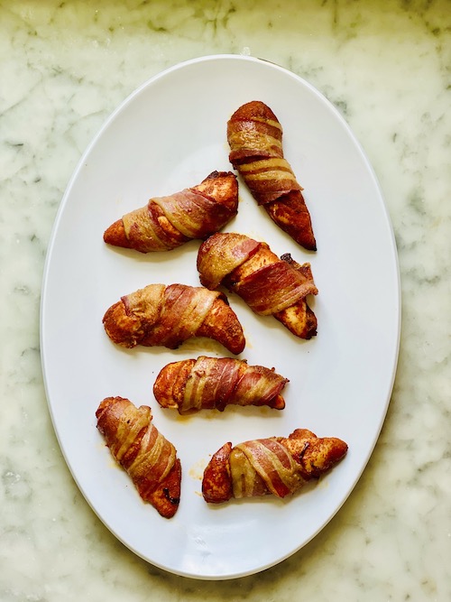 Bacon wrapped chicken tenders on a white serving platter.