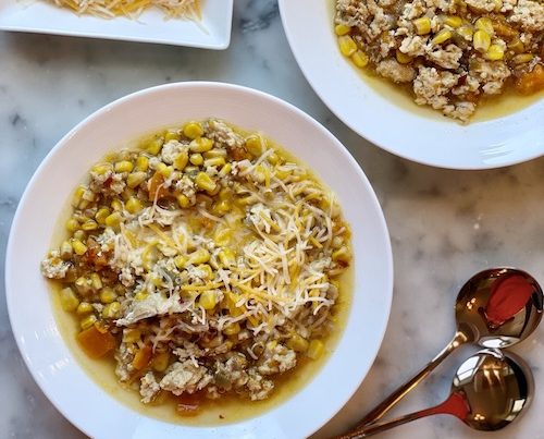 Two white bowls of spicy chicken and corn chili on a counter.