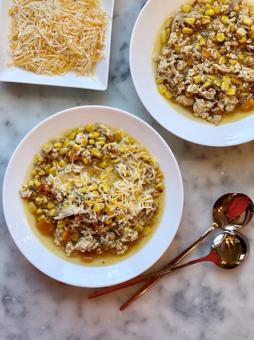 Two white bowls of spicy chicken and corn chili on a counter.
