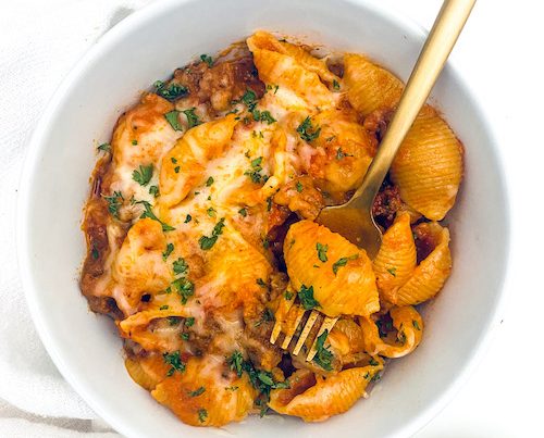 Cheesy Ground Beef + Shells in a small white bowl with a golden fork.