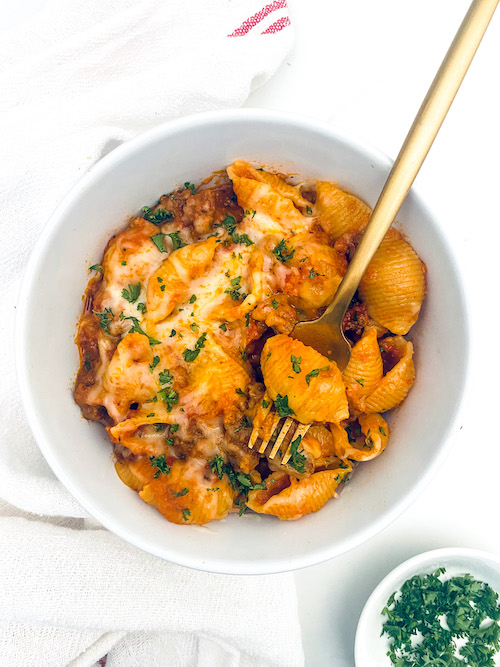 Cheesy Ground Beef + Shells in a small white bowl with a golden fork.