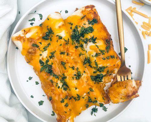 Chicken Tinga Enchiladas on a plate with a golden fork.