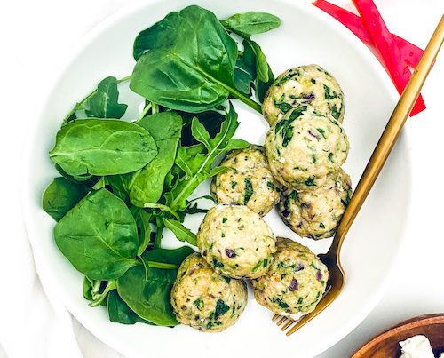 Spinach + Feta Turkey Meatballs next to fresh spinach on a white plate.