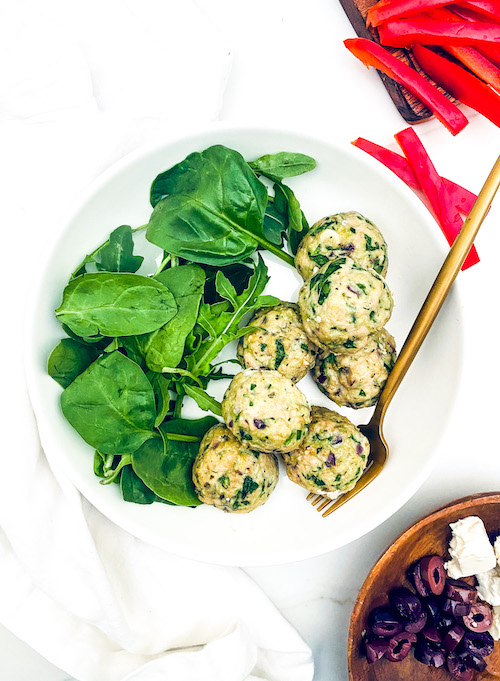Spinach + Feta Turkey Meatballs next to fresh spinach on a white plate.