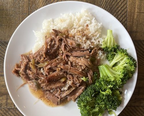 Apple cider braised shredded pork with white rice and broccoli on a white plate.