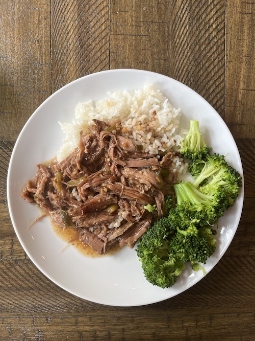 Apple cider braised shredded pork with white rice and broccoli on a white plate.