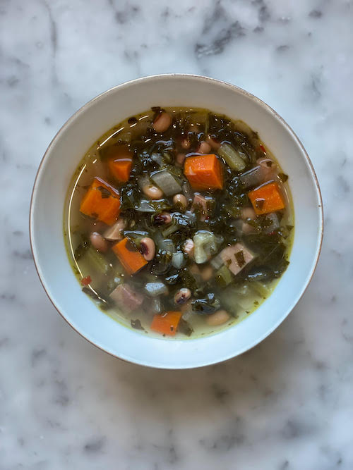Black eyed pea soup with ham in a white bowl.