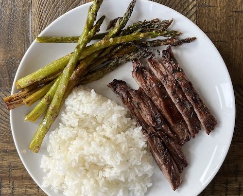 Chimmichurri steak slices with white rice and asparagus on a white plate.
