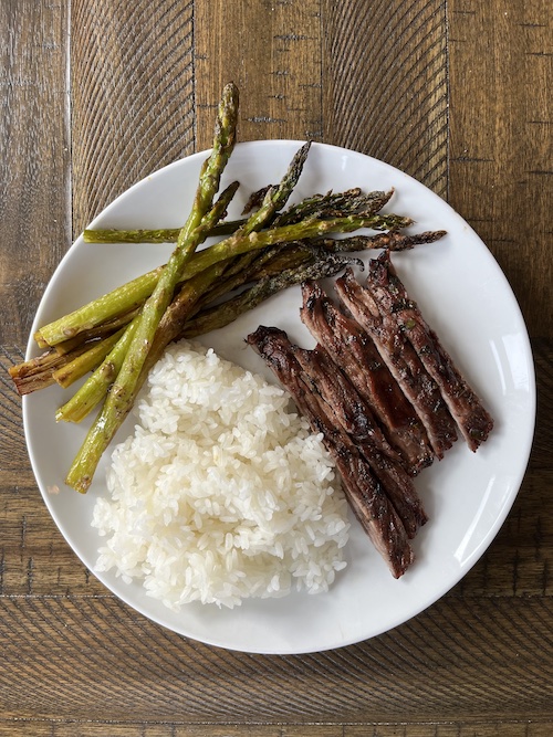 Chimmichurri steak slices with white rice and asparagus on a white plate.