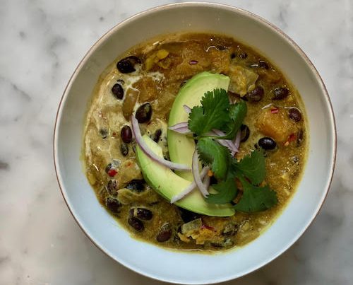 Coconut Ginger Black Bean soup in a white bowl, topped with avocado.