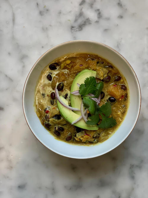 Coconut Ginger Black Bean soup in a white bowl, topped with avocado.