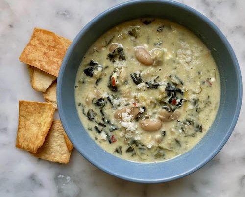 A blue bowl filled with spinach artichoke white bean stew.