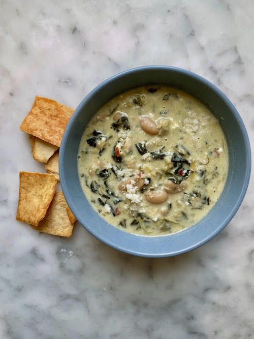 A blue bowl filled with spinach artichoke white bean stew.
