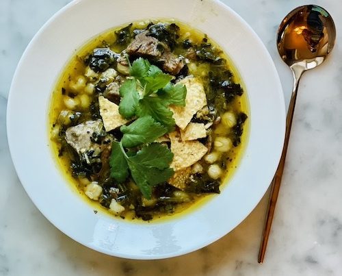 Green pork pozole topped with chips in a white bowl.