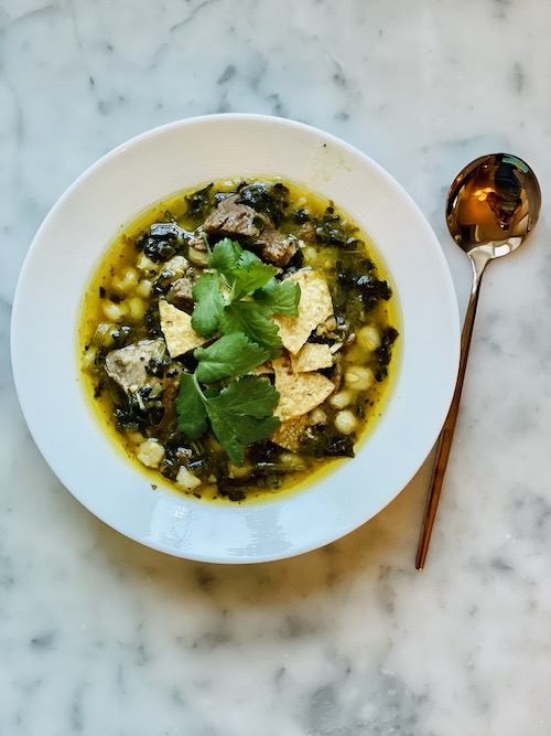 Green pork pozole topped with chips in a white bowl.