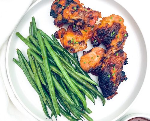 Apricot glazed chicken wings and green beans on a white dinner plate.