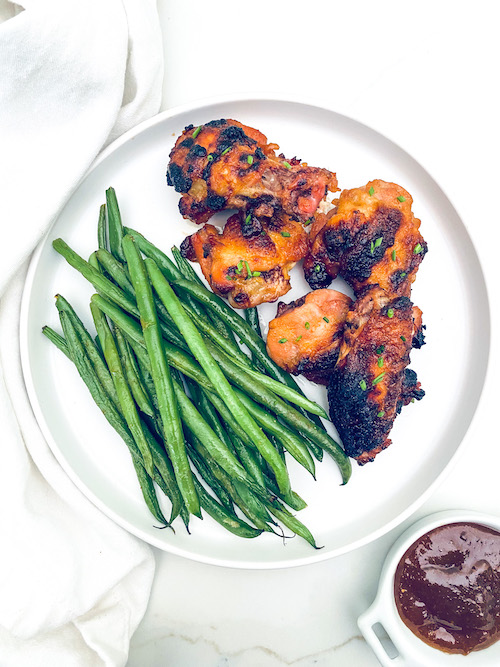 Apricot glazed chicken wings and green beans on a white dinner plate.