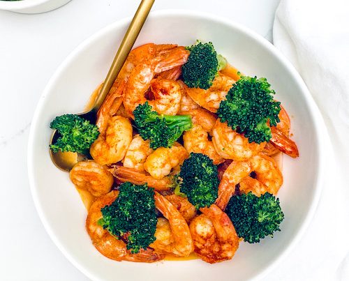 Garlic shrimp and broccoli with a spoon in a large white bowl;