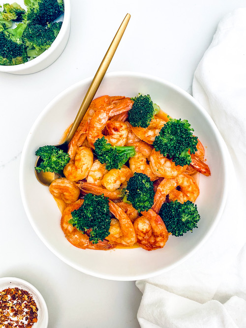Garlic shrimp and broccoli with a spoon in a large white bowl;