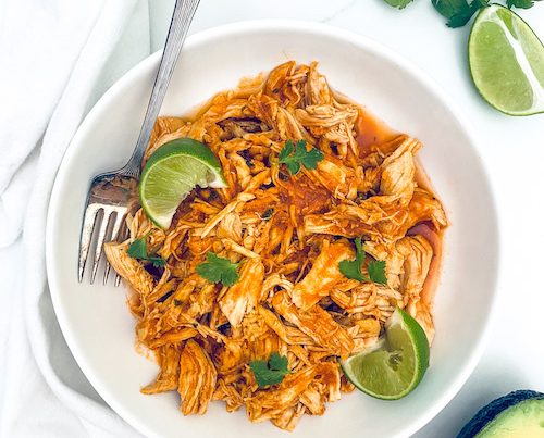 Spicy Latin-style pulled chicken with a fork in a white bowl.