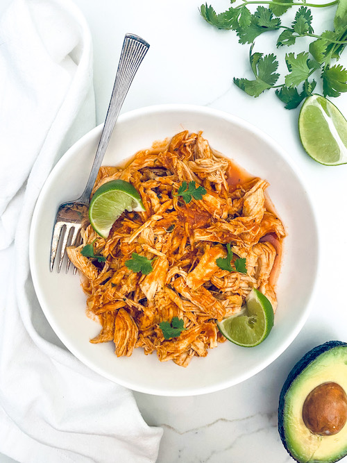Spicy Latin-style pulled chicken with a fork in a white bowl.