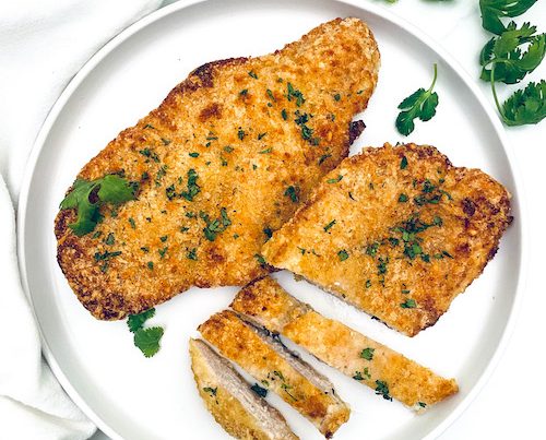 Parmesan crusted chicken cutlets on a white dinner plate.