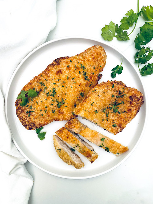 Parmesan crusted chicken cutlets on a white dinner plate.