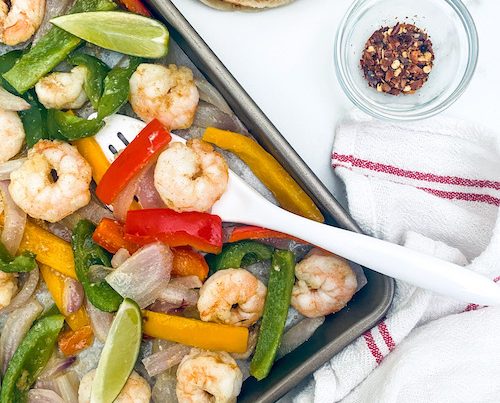 Shrimp, peppers, and limes on a baking sheet.