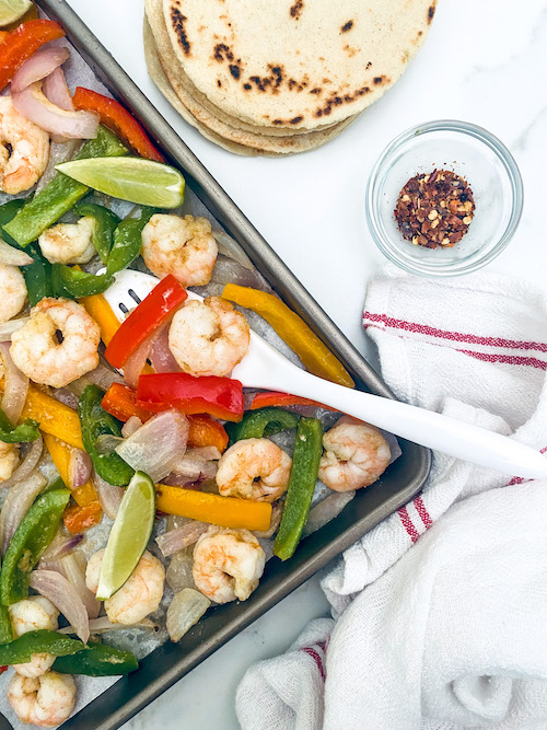 Shrimp, peppers, and limes on a baking sheet.