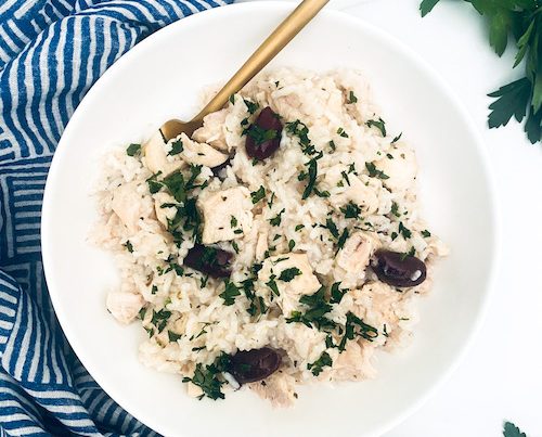 Greek chicken and olives over rice in a white bowl.