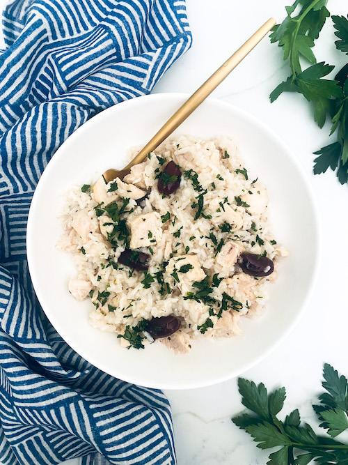 Greek chicken and olives over rice in a white bowl.