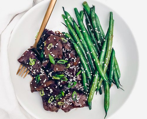 Mongolian beef and string beans on a white dinner plate.