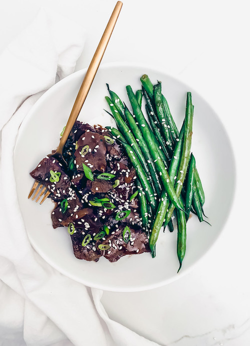 Mongolian beef and string beans on a white dinner plate.