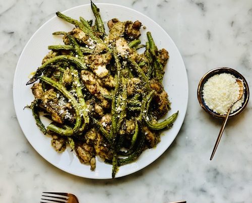 Pesto chicken and green beans on a large white dinner plate.