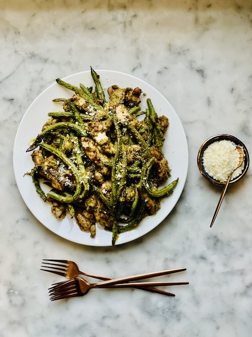 Pesto chicken and green beans on a large white dinner plate.