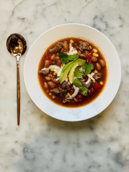 A white bowl filled with spicy beef and bean stew topped with avocado.