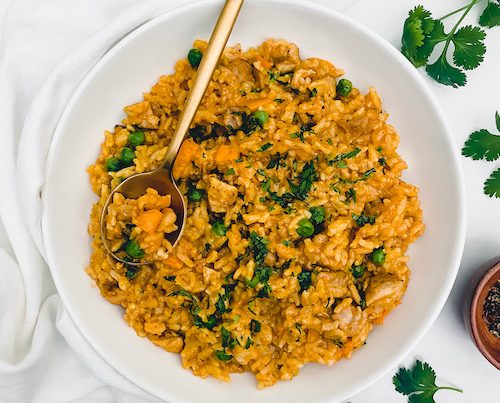 A large white bowl of arroz con pollo with a gold spoon.