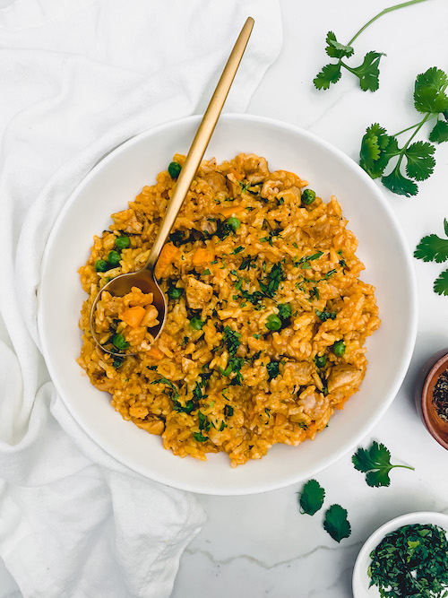A large white bowl of arroz con pollo with a gold spoon.