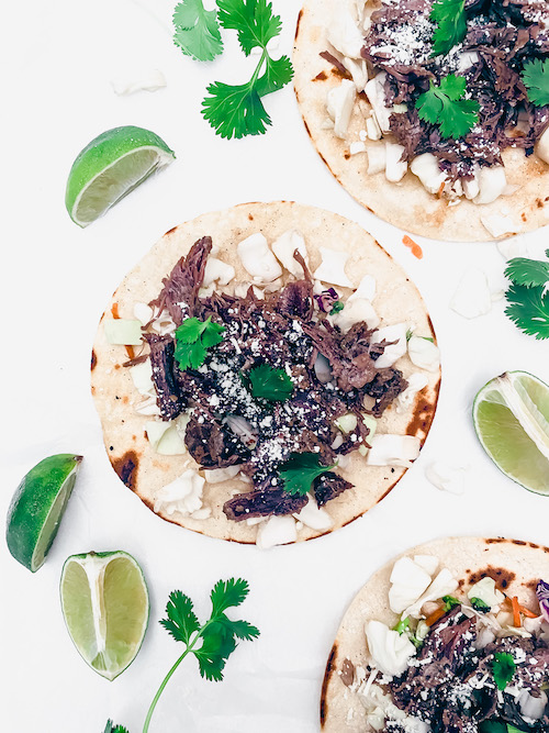 Barbacoa beef with onions on tortillas on a white surface.