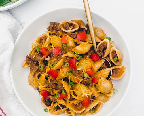 Homemade cheesy hamburger helper in a white bowl with gold spoon.