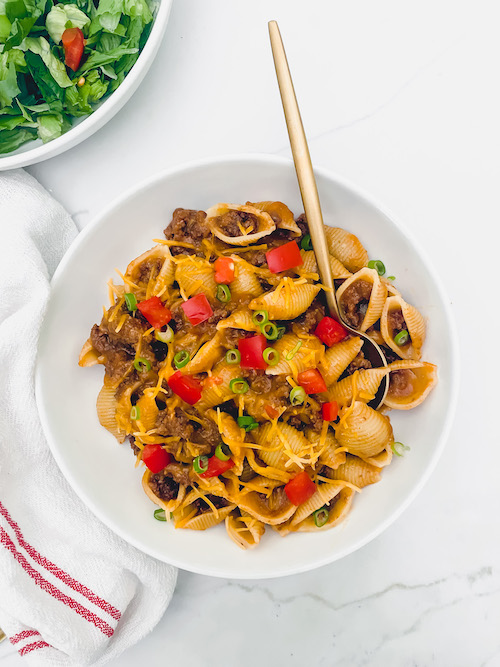 Homemade cheesy hamburger helper in a white bowl with gold spoon.