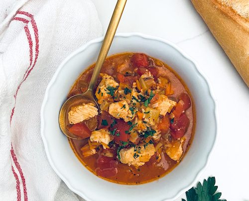 Chicken tomato and rice soup in a white bowl with a gold spoon.