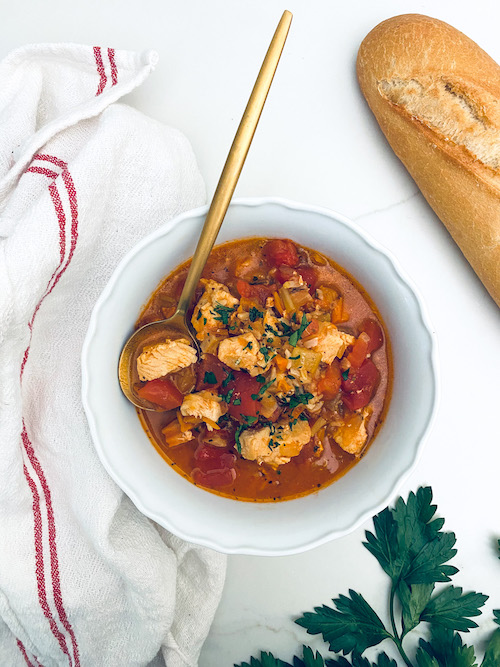 Chicken tomato and rice soup in a white bowl with a gold spoon.