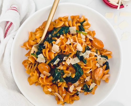 Creamy sausage spinach pasta in a white bowl with gold fork.